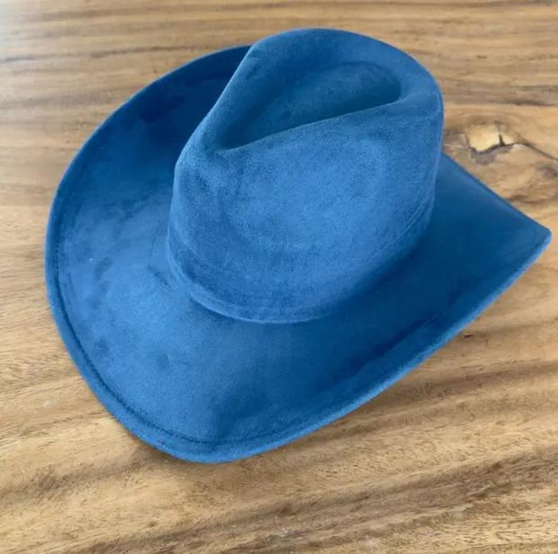 May include: A solid blue cowboy hat with a soft, matte, suede-like texture. The hat features a pinched crown and a wide, curved brim. The design is uniform in colour, showcasing a deep blue hue across the entire exterior surface of the hat.