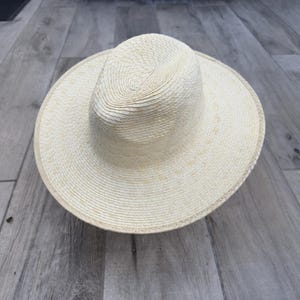 May include: A wide-brimmed straw hat with a cream color. The hat has a woven texture and a slightly rounded crown.
