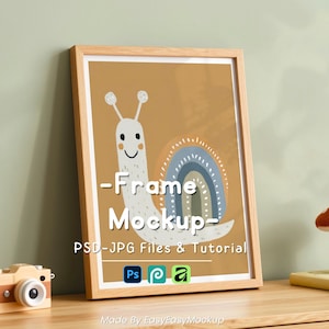 May include: A framed print featuring a whimsical snail illustration with a rainbow and the text "-Frame Mockup-". The frame is made of light wood. A toy camera and a mushroom decoration are on the wooden surface.