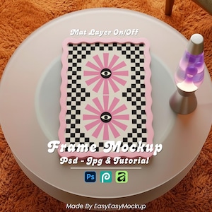 May include: A pink and black framed artwork with a retro eye design sits on a round table. A lava lamp with a purple liquid is next to the frame. The table is on an orange shag rug. Text on the frame says "Frame Mockup".