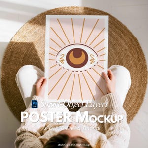 May include: A poster mockup with a brown and beige eye design and radiating lines. The poster is held by a person. The text "POSTER Mockup" is visible on the poster. The image is on a woven rug. The poster is a JPG-PSD file.