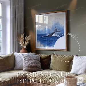 May include: A framed watercolor painting of a whale tail breaching the water, hanging on a green wall in a living room setting. The painting is in a wooden frame and is surrounded by a brown couch with pillows.