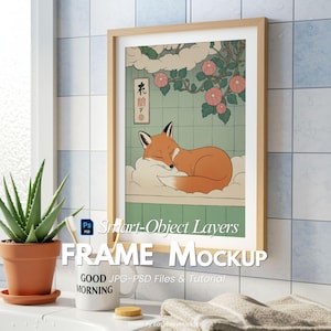 May include: A framed art print featuring a sleeping fox illustration in warm tones. The artwork is set in a light wood frame. The text "FRAME MOCKUP" is visible. A potted aloe plant and a mug that says "MORNING" are in the foreground.