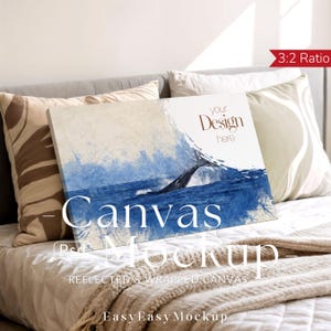 以下が含まれることがあります： クジラが海から現れる様子を描いたキャンバスモックアップ。青と白の水彩画風アートワーク。キャンバスは枕と毛布のあるベッドに立てかけられています。キャンバスには「Your Design Here」と「Canvas Mockup」と書かれています。