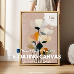 Può includere: Stampa su tela incorniciata con un design floreale. I fiori bianchi, arancioni e blu risaltano su uno sfondo rosa. La cornice è in legno chiaro. Il testo recita "FLOATING CANVAS" e "Smart-Object Layers".