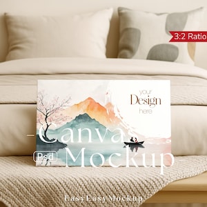 以下が含まれることがあります： 山、湖、ピンクの花が咲く木を描いた水彩画の風景画が特徴のキャンバスモックアップ。キャンバスには「Your Design here」と「Canva Mockup」の文字が表示されています。画像はベッドに置かれています。