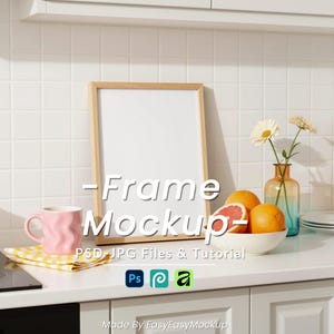 May include: A wooden frame mockup with the text "-Frame Mockup-" is propped against a white tiled wall in a kitchen setting. A pink mug, fruit, and flowers are on the counter. The image includes PSD, JPG files, and a tutorial.