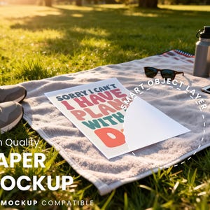 May include: A picnic scene with a soccer ball, sunglasses, a water bottle, and a smartphone on a towel. A paper mockup with the text "SORRY I CAN'T I HAVE PLANS WITH D" is displayed. Sneakers are in the foreground.