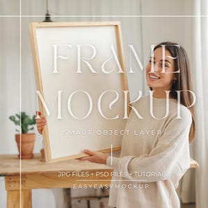 May include: A woman holds a wooden frame mockup with a white background. The frame is large and the woman is smiling. The text "FRAME MOCKUP" is written in white on the frame. The text "SMART OBJECT LAYER" is written in white below the frame. The text "JPG FILES + PSD FILES + TUTORIAL" is written in white below the frame. The text "EASYEASYMOCKUP" is written in white below the frame.