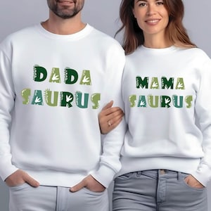 May include: White sweatshirts with green and white text that reads "Dada Saurus" and "Mama Saurus".
