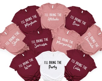 May include: Set of ten t-shirts in maroon and blush pink with white text. Each shirt says "I'll bring the" followed by a different phrase, such as "shots", "mayhem", "attitude", "beer", "chocolate", "sarcasm", "wine", "margaritas", "party", and "calm".