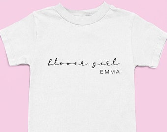 May include: White t-shirt with the text "flower girl" and the name "EMMA" printed on it.