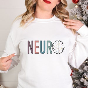 a woman wearing a neuro sweatshirt standing in front of a christmas tree