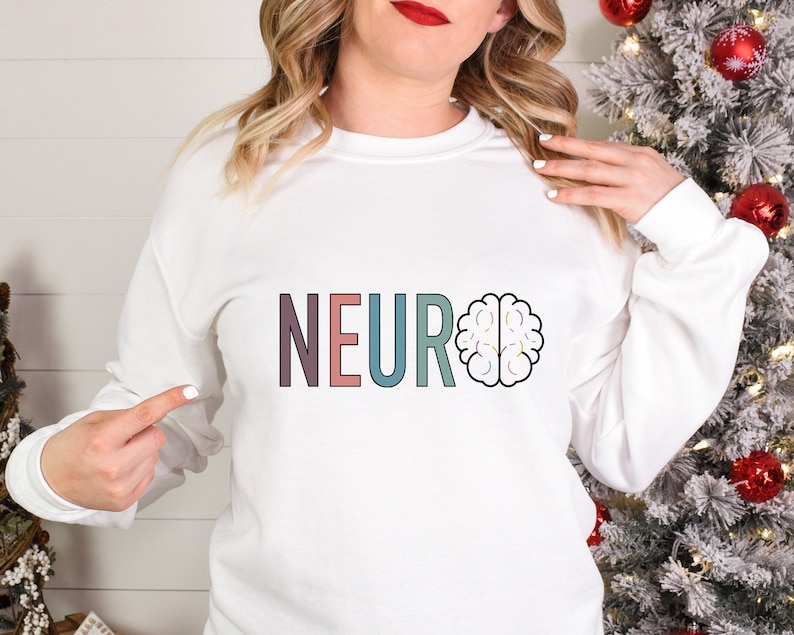 a woman wearing a neuro sweatshirt standing in front of a christmas tree