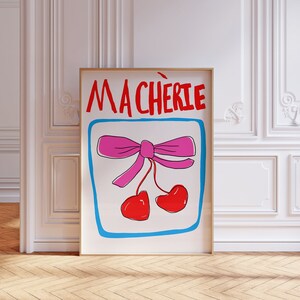 May include: A framed print with a white background and a pink bow with two red cherries. The text "MA CHERIE" is written in red letters at the top of the print.