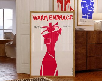 May include: A framed art print with the words "WARM EMBRACE" in red, along with an abstract red figure on a white background. Two other framed prints are visible, one with red sandals and another with blue geometric shapes. The artwork is displayed in a room with wooden floors.