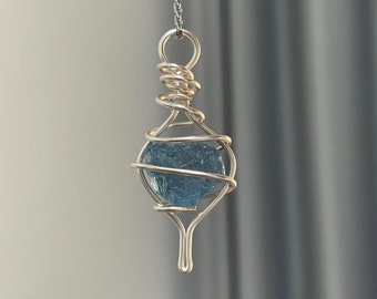 May include: A silver wire wrapped pendant necklace featuring a light blue gemstone. The pendant is shaped like a teardrop and hangs from a delicate silver chain.