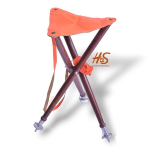 May include: A wooden folding stool with an orange canvas seat and a brown strap. The stool has three legs with metal tips.