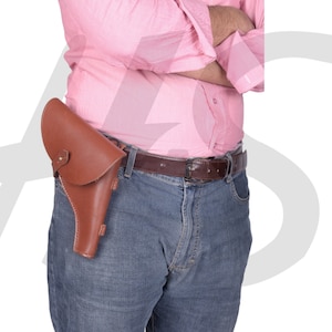 May include: A brown leather holster with a metal buckle is worn on a person's belt. The holster is secured to a belt with a brown leather strap.