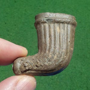 May include: A brown, weathered clay tobacco pipe bowl featuring a vertical ribbed design on the upper section and a textured, floral-like relief pattern along the lower curve, showing signs of age and surface wear throughout the material.