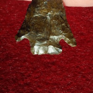 May include: A dark brown arrowhead with a pointed tip and two notches on the sides. The arrowhead has a rough, textured surface.