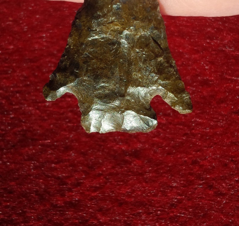 May include: A dark brown arrowhead with a pointed tip and two notches on the sides. The arrowhead has a rough, textured surface.