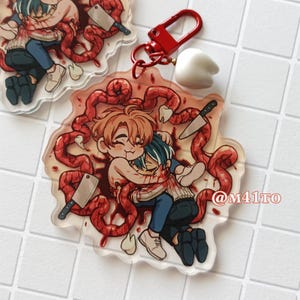 Puede incluir: Llavero acrílico transparente con una ilustración de estilo anime de dos figuras abrazándose, rodeadas de formas rojas en forma de intestino y cuchillos. Se adjunta un cierre rojo y un dije de diente blanco. El texto "@M41TO" es visible.