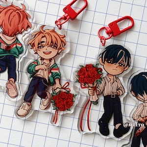 Könnte beinhalten: Acryl-Anhänger mit Anime-Charakteren, die rote Rosensträuße halten. Die Charaktere haben verschiedene Haarfarben und tragen Freizeitkleidung. Rote Karabiner-Schlüsselanhänger sind ebenfalls zu sehen. Der Hintergrund ist ein weißes Gitter.