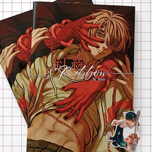 Puede incluir: Varias copias de un cómic manga titulado "Ribbon" con una ilustración estilizada de una persona con manos y cadenas rojas. La portada presenta texto japonés y el nombre del autor, "Maito."