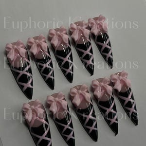 May include: Ten black and pink ballerina-themed nail tips with pink bows.