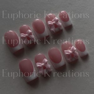 May include: Pink and white fake nails with a pink bow accent on each nail.