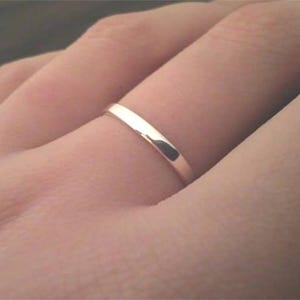 Pode incluir: Um close-up de um anel de prata em um dedo. O anel é fino e tem uma superfície lisa e reflexiva. O anel é uma banda simples, provavelmente uma aliança de casamento ou um anel de noivado.