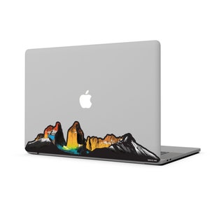 K&ouml;nnte beinhalten: Ein silberner Laptop mit einem bunten Bergbandsticker auf der R&uuml;ckseite. Der Sticker hat einen schwarzen Umriss und eine Vielzahl von Farben, darunter Gelb, Orange, Rot, Blau und Gr&uuml;n.