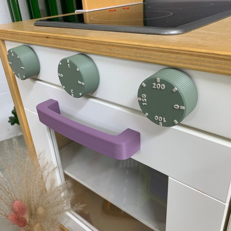 Drehknöpfe für Kinderküche Duktig von IKEA in der Farbe sanftes Grün mit hellgrauer Beschriftung. 2 Drehknöpfe für den Herd und 1 Drehknopf für den Ofen