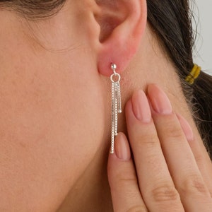 May include: Silver dangle earrings with multiple chains hanging from a small ball at the top.