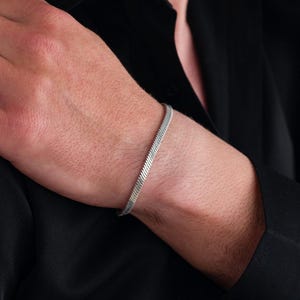 Puede incluir: Un brazalete de cadena de plata con un diseño de cadena de serpiente.