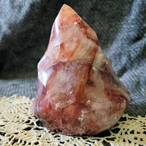 May include: A polished flame-shaped crystal carving featuring a mix of translucent white and deep reddish-brown inclusions. The stone has a smooth, glossy surface with visible internal fractures and natural mineral patterns throughout the structure.