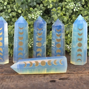 May include: Six blue and yellow moon phase crystal points on a wooden surface. The crystals are clear and have a gold moon phase design.