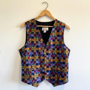 Puede incluir: Un chaleco sin mangas con un vibrante patrón de tablero de ajedrez multicolor en tonos azul, rojo, amarillo y verde. La prenda tiene un escote en V, un forro interior negro y cinco pequeños botones dorados en el cierre frontal.