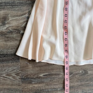 May include: A pale peach-colored skirt with a flared, flowing silhouette. A pink measuring tape is placed vertically along the fabric, showing a length measurement extending from 39 inches down to 54 inches along the hemline of the garment.