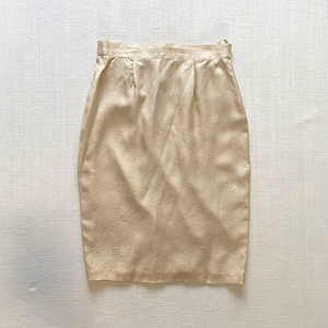 May include: A beige pencil skirt with a textured pattern. The skirt is knee-length and has a tailored fit. The fabric has a subtle sheen, and the skirt appears to be made of a lightweight material. The skirt is suitable for various occasions.