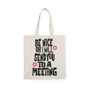 May include: A beige tote bag with black text that reads "Be nice or I will send you to a meeting" with pink flower accents.