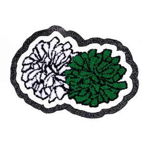Könnte beinhalten: Ein dekorativer Aufnäher mit zwei stilisierten floralen Designs. Eines ist weiß mit schwarzen Umrissen, das andere ist grün. Der Aufnäher hat einen schwarzen Glitzerrahmen und einen weißen Hintergrund.