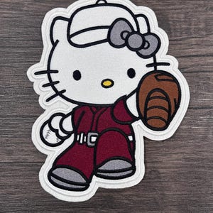 Peut inclure: Patch brodé blanc de Hello Kitty portant une casquette de baseball, un uniforme marron et tenant un gant de baseball marron.
