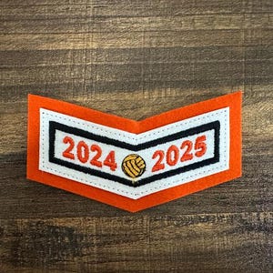 Puede incluir: Parche de chevron de fieltro naranja y blanco con costuras negras y texto blanco que dice "2024" y "2025" con un balón de baloncesto amarillo y naranja en el centro.