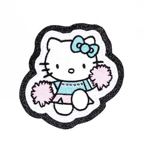 Puede incluir: Parche blanco bordado de Hello Kitty vestida de animadora, sosteniendo pompones rosas, con un lazo azul en la cabeza.