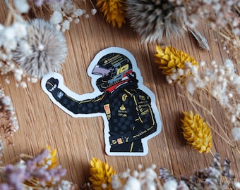 May include: A black and gold sticker of a race car driver wearing a helmet and raising their fist in the air.