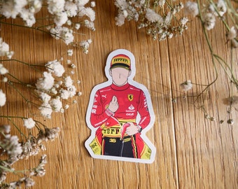May include: A red and yellow racing driver sticker with the Ferrari logo and the number 16. The driver is wearing a red racing suit with a yellow helmet.