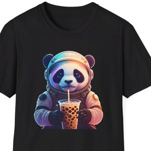May include: Black t-shirt with a panda bear illustration. The panda is dressed in an astronaut suit and helmet, holding a bubble tea. The design is colourful and detailed, with the panda's fur in black and white. The panda is drinking from a clear cup.
