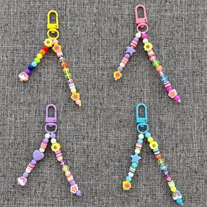 May include: Four colorful beaded keychains with different charms. Each keychain features a rainbow, a star, a heart, and a smiley face. The keychains are made with colorful beads and metal clasps.